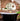 A bathroom wall with red rustic brick slips, a semi circular mirror above a black curved top bath. Green houseplant leaves are on the right.