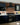 A navy kitchen with white worktop is either side of a black range cooker and extractor. Red brick slips clad the wall behind.