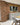 A pale orange brick kitchen, with a column and wall covered around a window. grey kitchen units with a white worktop.
